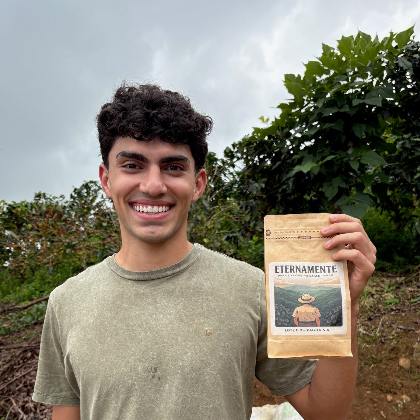 Man holding a coffee package labeled 'Eternamente' in a coffee plantation.